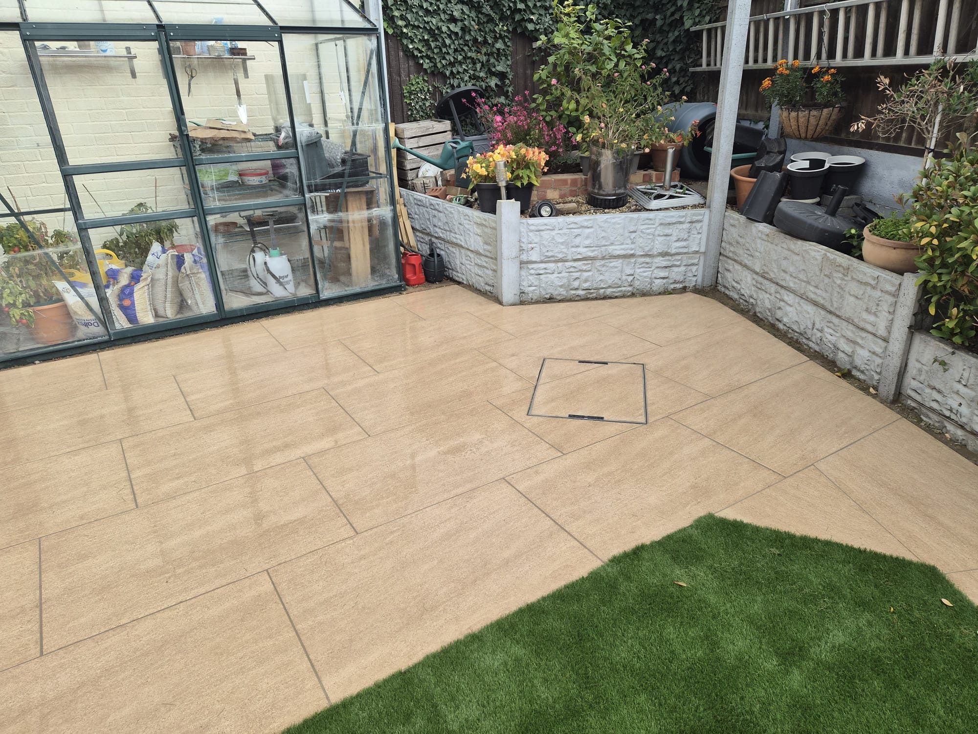 Beige porcelain patio by a greenhouse with artificial grass