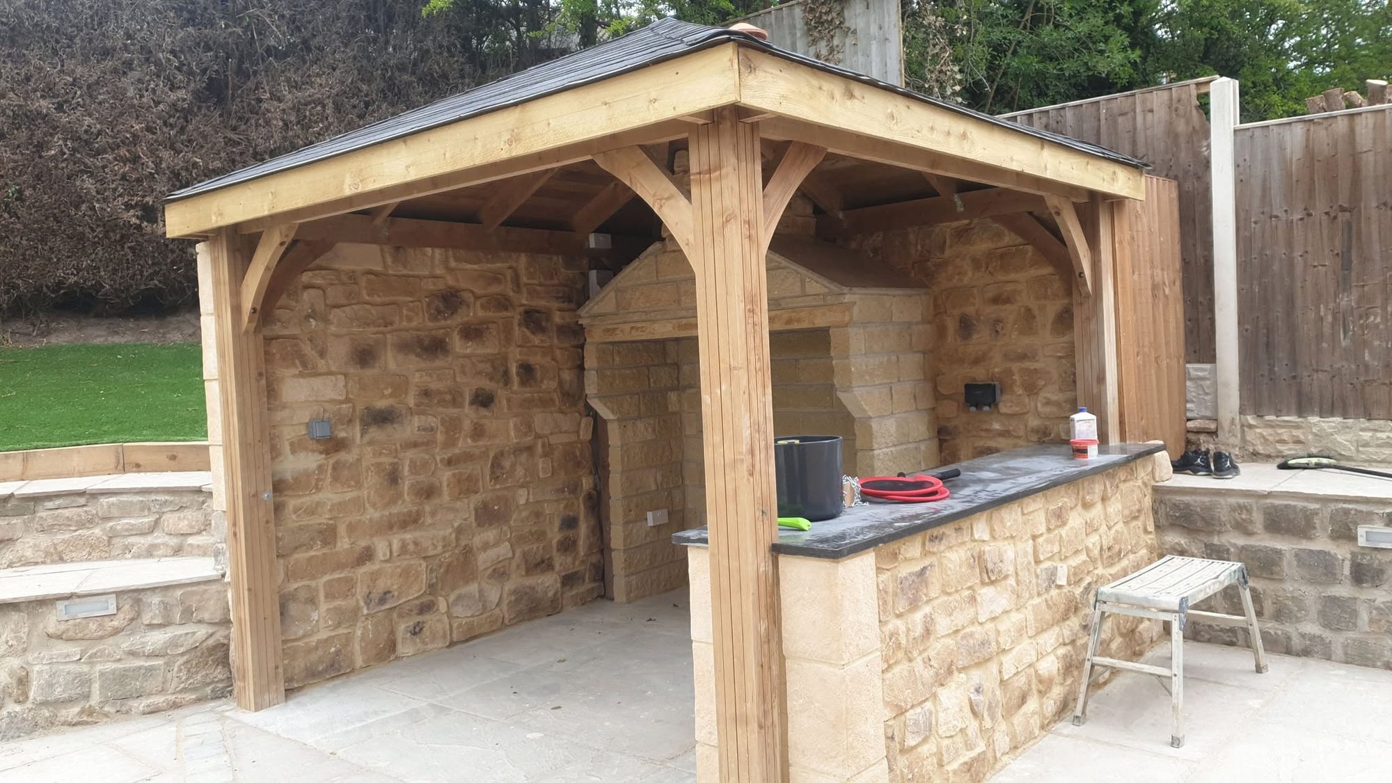 Timber gazebo over a stone outdoor kitchen with surrounding paving