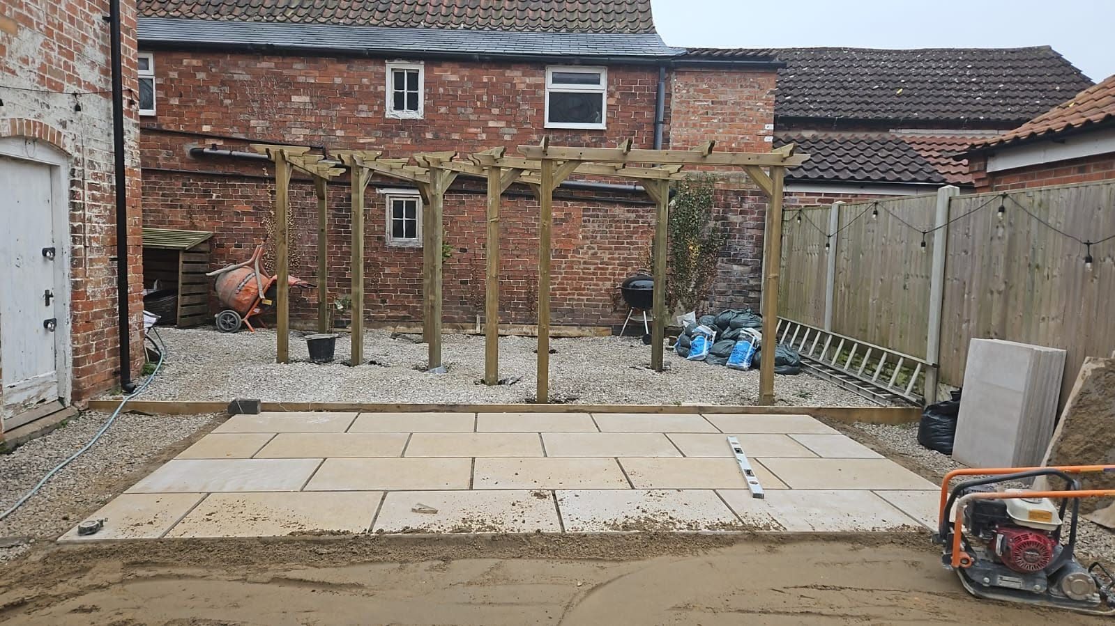 Patio installation in progress with paving slabs and a plate compactor