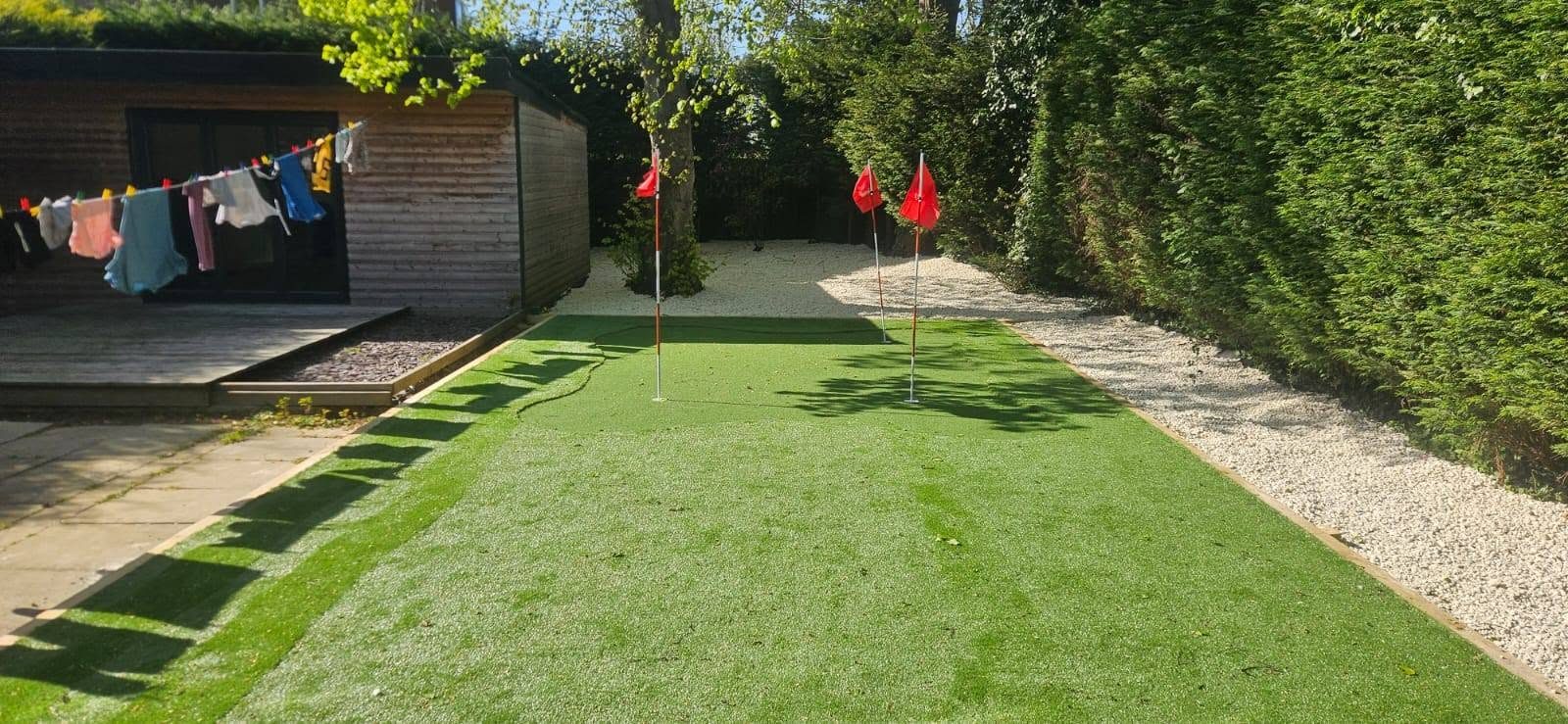 Artificial grass putting green with red flags beside a timber garden shed