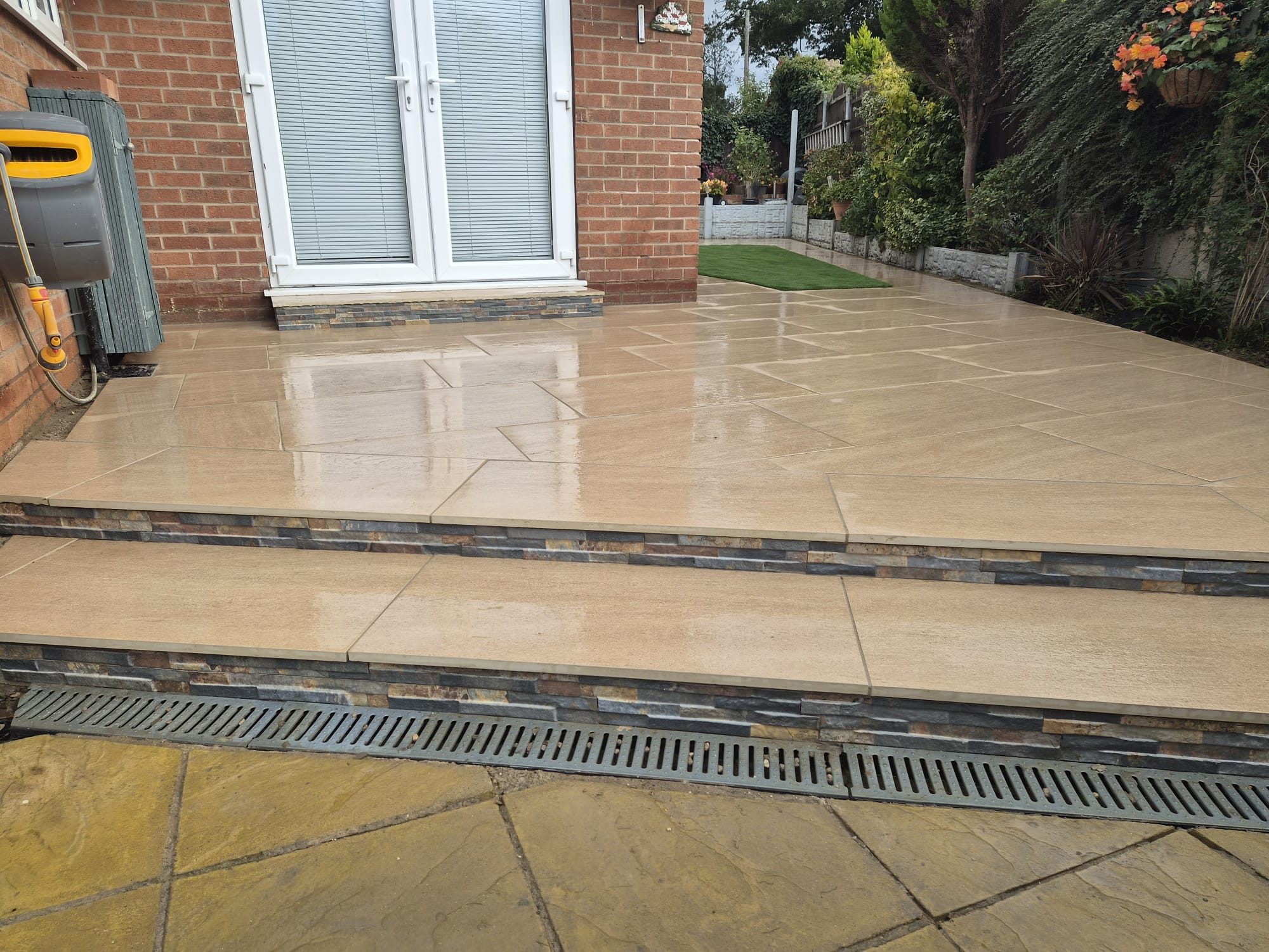 Beige porcelain patio with steps and a linear drainage channel outside French doors