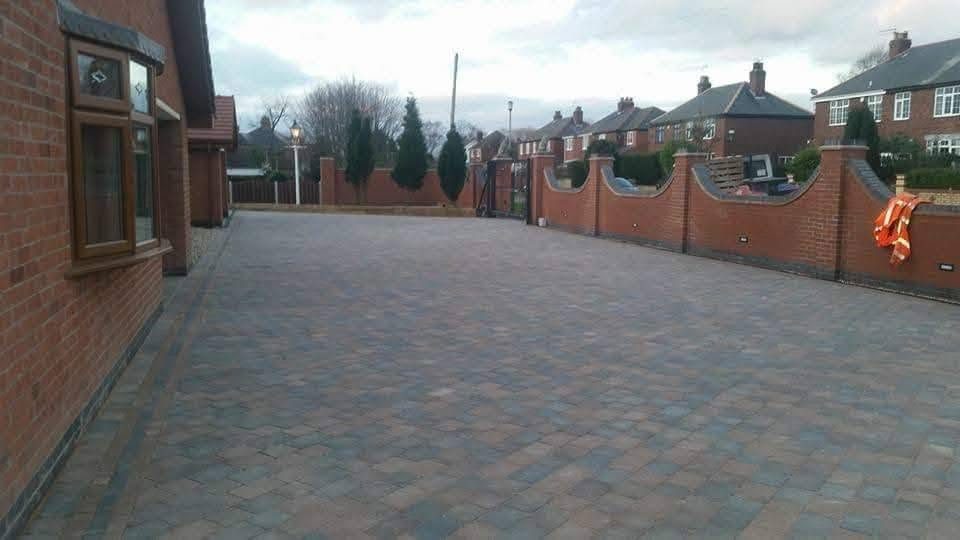 Large multi-tone block paving driveway beside a brick house